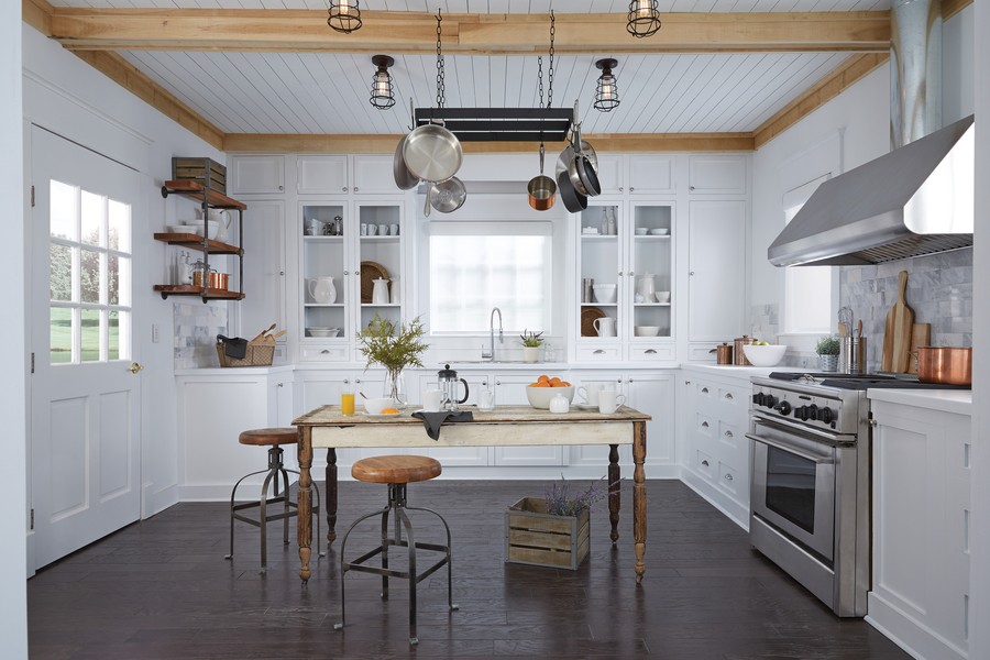 Light gleaming into a white kitchen with a wooden table in the middle. 