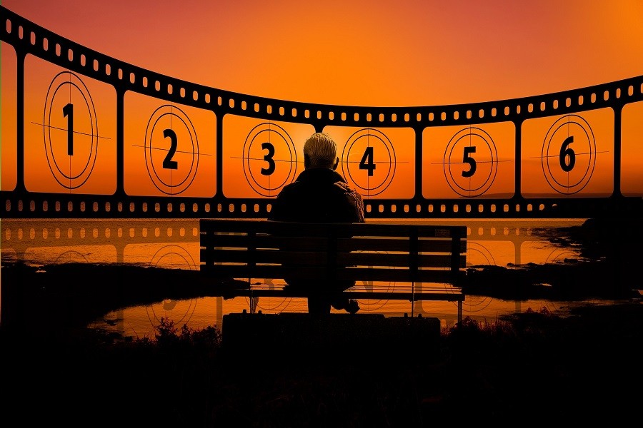 Stylized image of a person sitting on a park bench with frames of a film leader countdown spread in front of them.