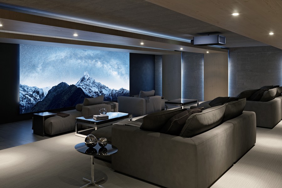 The interior of a luxury home theater featuring a large screen on the wall with two tiers of gray lounge seats facing the screen. 