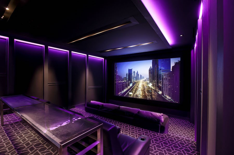 A home cinema with a large screen, tiered seating, and custom lighting designed by a professional home theater company in Denver.