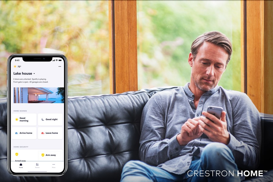 A man sits on his couch, controlling his Colorado smart home from the Crestron Home app on his smartphone. 