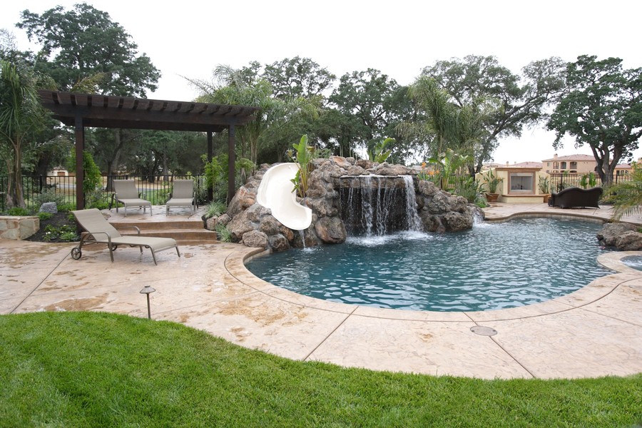  A Denver backyard with an outdoor sound system featuring a pool with a slide and waterfall, lounge chairs, and a pergola.